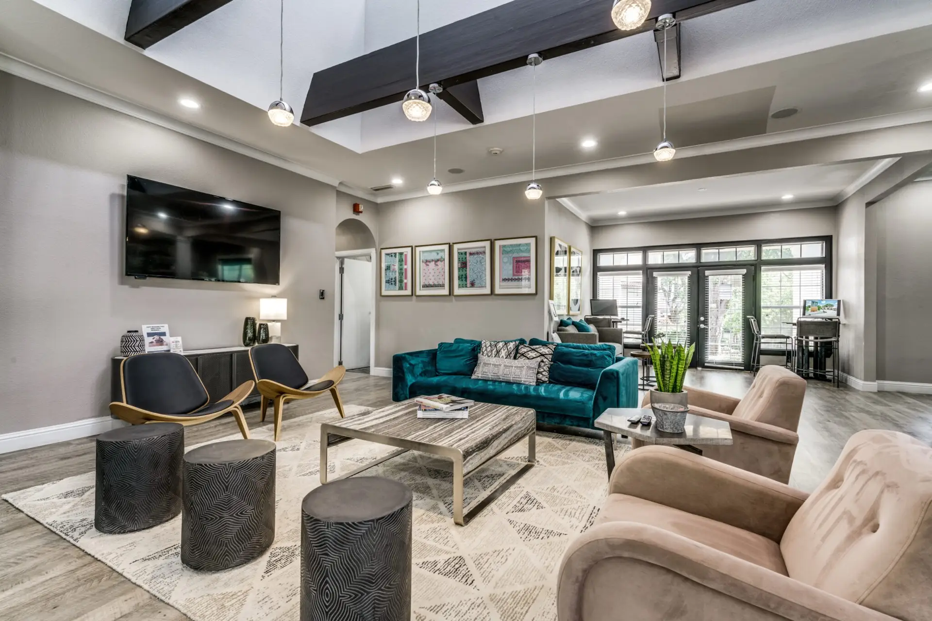 resident clubhouse with plush armchairs, a teal couch, stools, and designer chairs next to a wall mounted large screen TV.